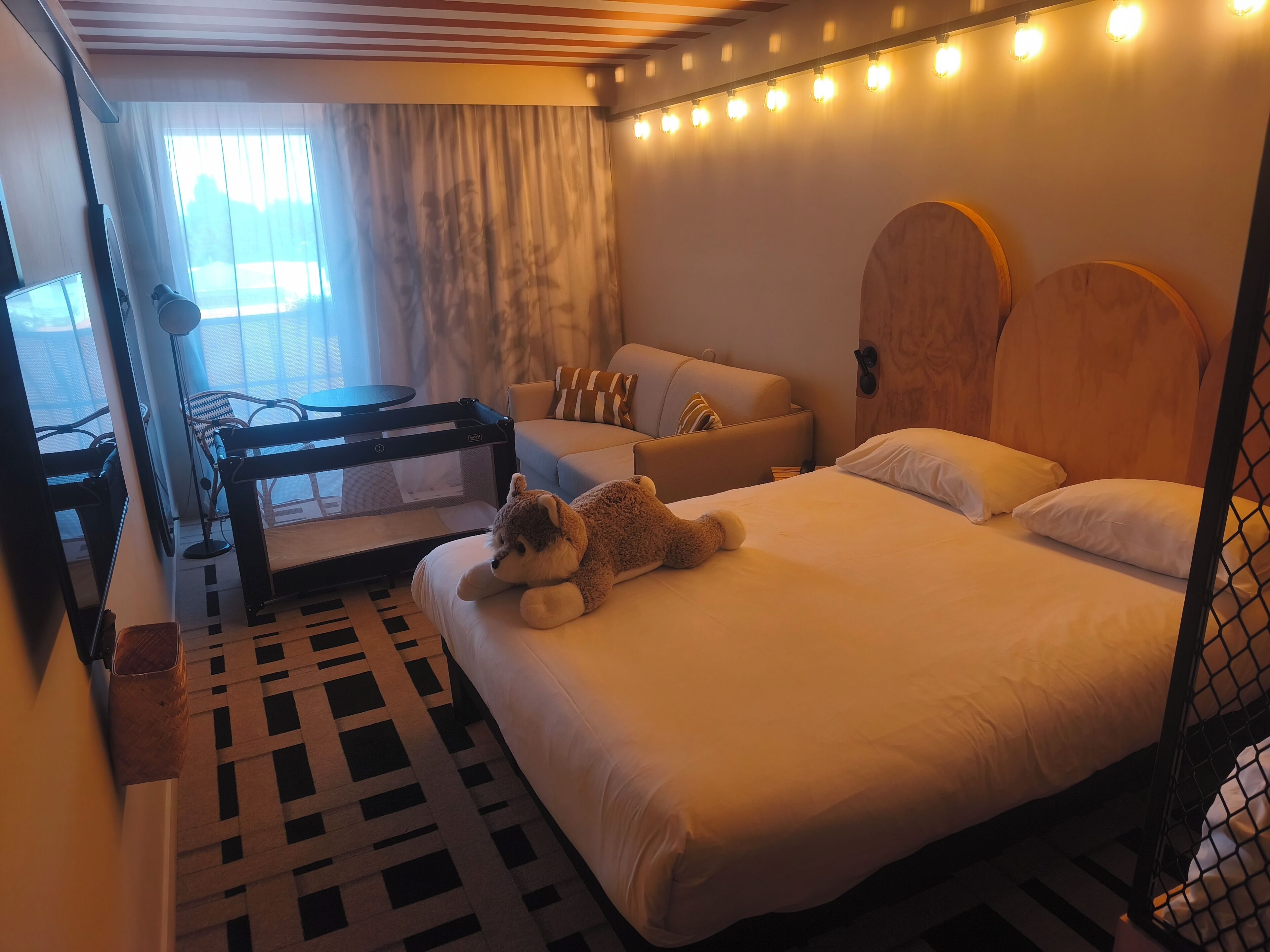 A hotel room with a bed, a sofa, a table, and a teddy bear.