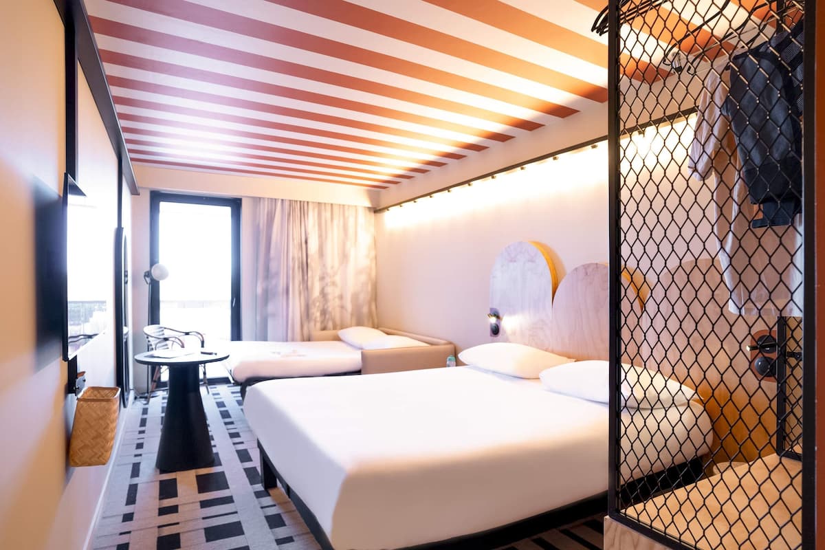 Ein Hotelzimmer mit Bett, kleinem Tisch, Stuhl, Fenster mit Vorhängen und Blick nach draußen.