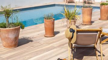 A poolside area with terracotta planters, a wooden lounge chair, and a pair of sandals.