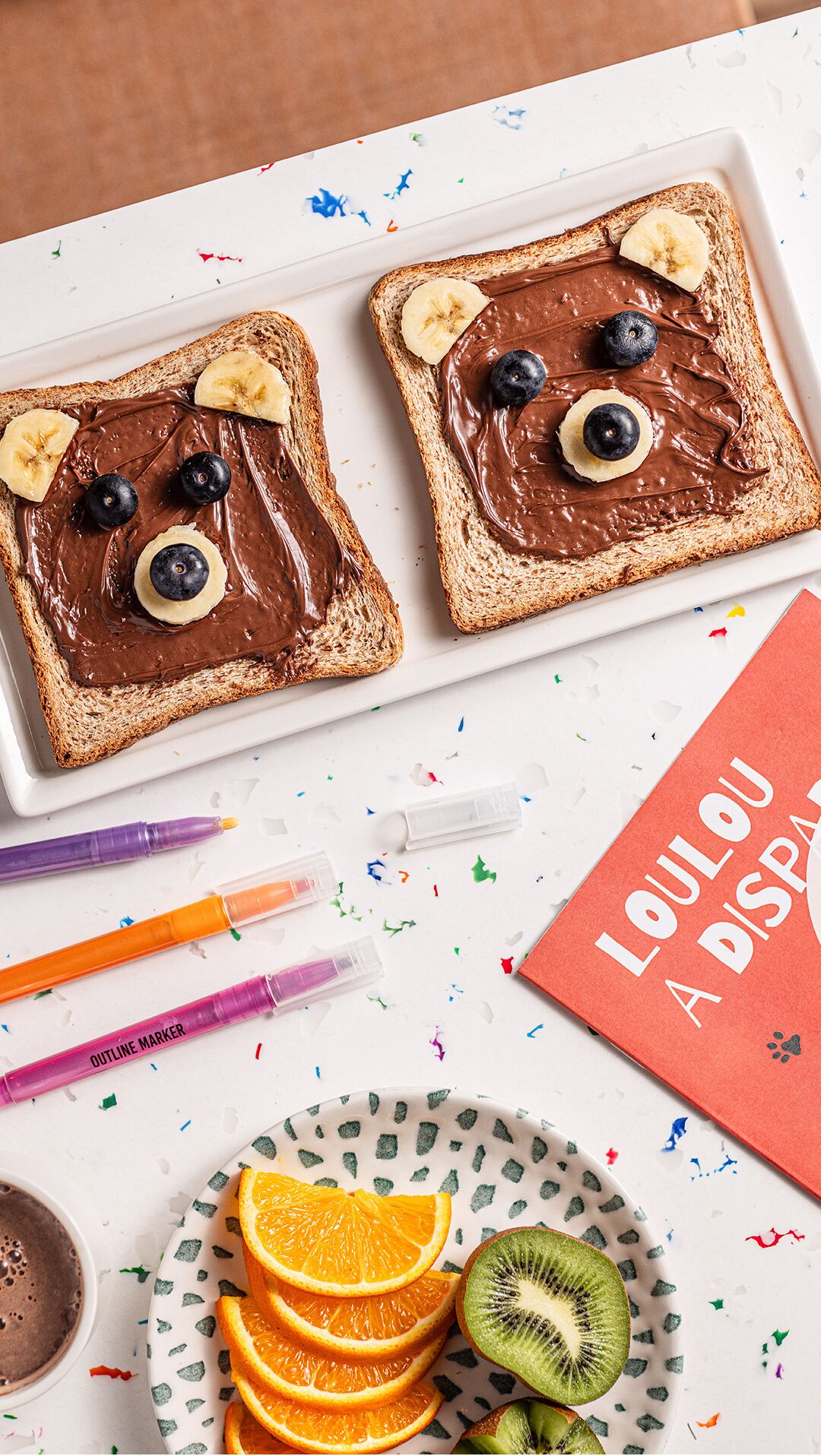 Dos tostadas con crema de chocolate, plátanos y arándanos dispuestos para simular un rostro.