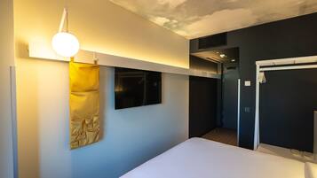 A modern hotel room with a bed, a wall-mounted TV, a hanging yellow towel, and a ceiling with a perforated design.