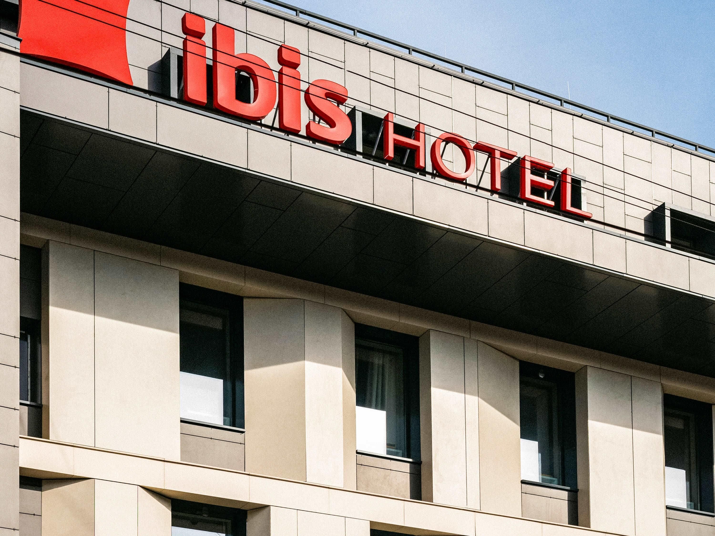 Une enseigne d’hôtel avec le nom « ibis HOTEL » écrit en grandes lettres rouges sur la façade d’un immeuble moderne.