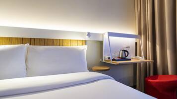Une chambre d’hôtel avec un lit, une table de chevet avec une lampe, une machine à café et un fauteuil rouge.