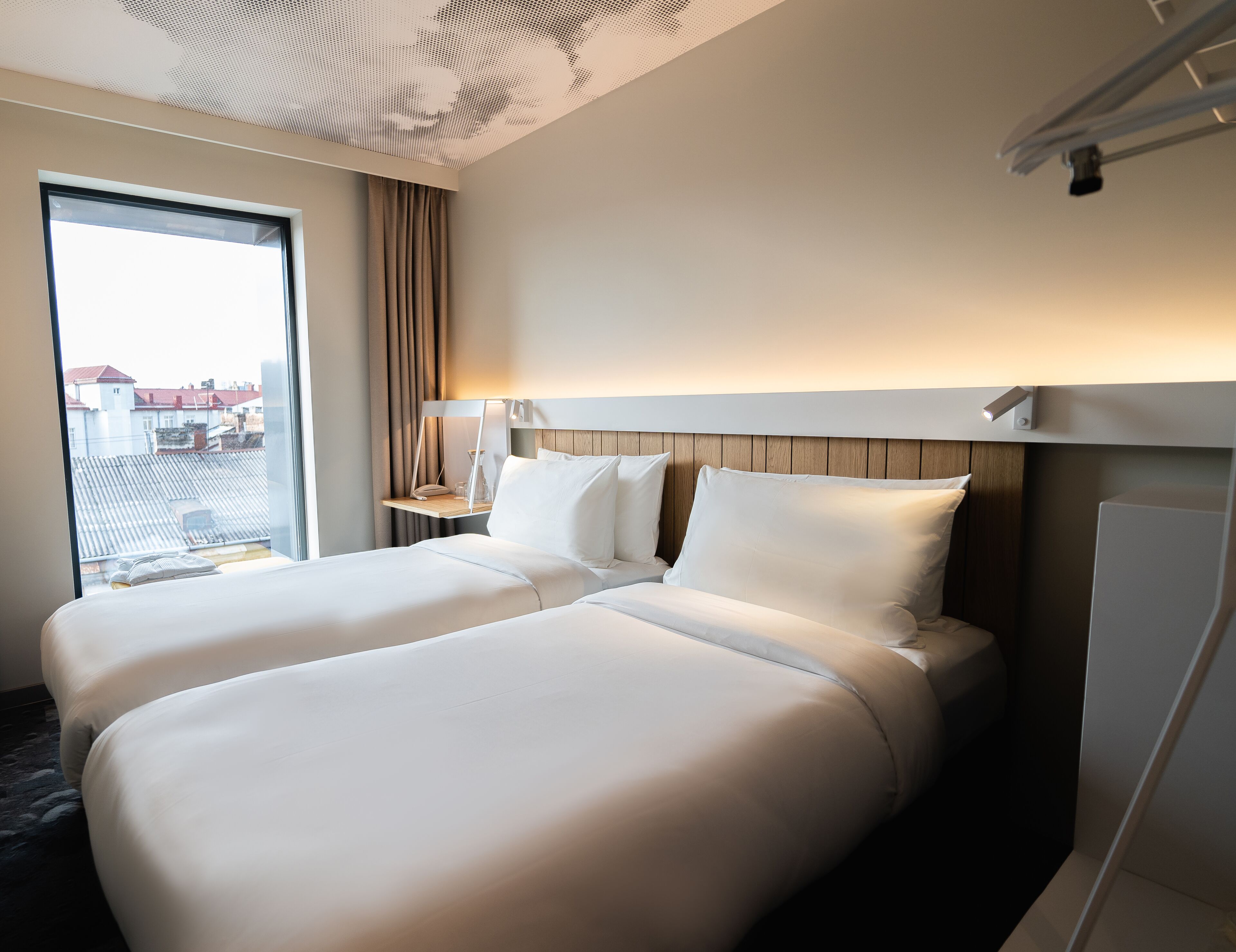 Una habitación de hotel con dos camas, una mesita de noche, una lámpara y vista a la ciudad.