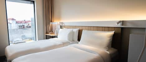 Quarto de hotel com duas camas, mesa de cabeceira, luminária e vista para a cidade.