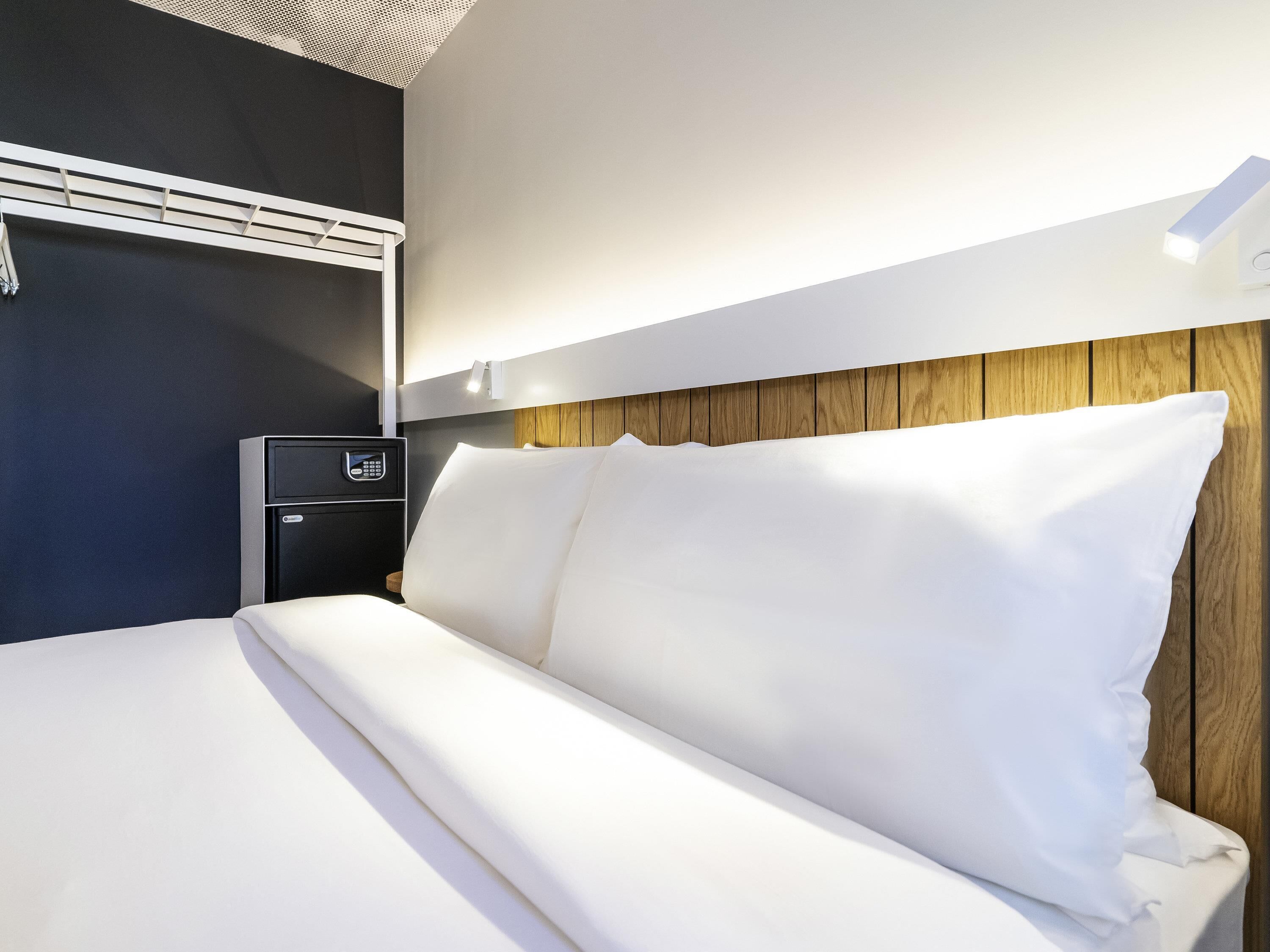 Een hotelkamer met een bed, een nachtkastje met een telefoon en een wandgemonteerde airconditioner.