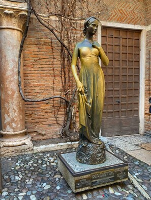 Una estatua de una mujer sobre un pedestal con una placa, frente a un muro de ladrillo y una puerta de madera.
