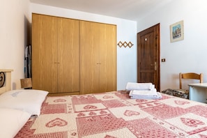 Ein Schlafzimmer mit großem Holzschrank, einem Bett mit gemustertem Überwurf und einem kleinen Tisch mit gefalteten Handtüchern.