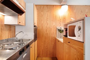 A compact kitchen with wooden cabinetry, a stainless steel stove, and a microwave. - Apartment "Nives" with Mountain View, Indoor Pool and Wi-Fi (Marilleva 1400)