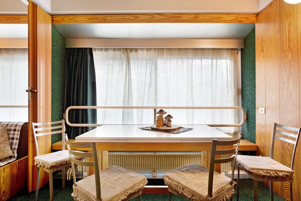 A compact room with a table and four chairs, a bench, and a window with curtains. - Apartment "Nives" with Mountain View, Indoor Pool and Wi-Fi (Marilleva 1400)
