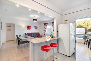 A modern kitchen with a central island, bar stools, a refrigerator, and a dining area with a sofa and chairs.