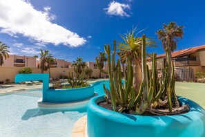 A pool area with blue planters, palm trees, and a clear blue sky.