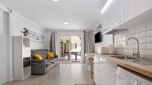 Ett modernt kök med en inbyggd diskmaskin, en matplats med bord och stolar samt ett vardagsrum med en soffa och kuddar.