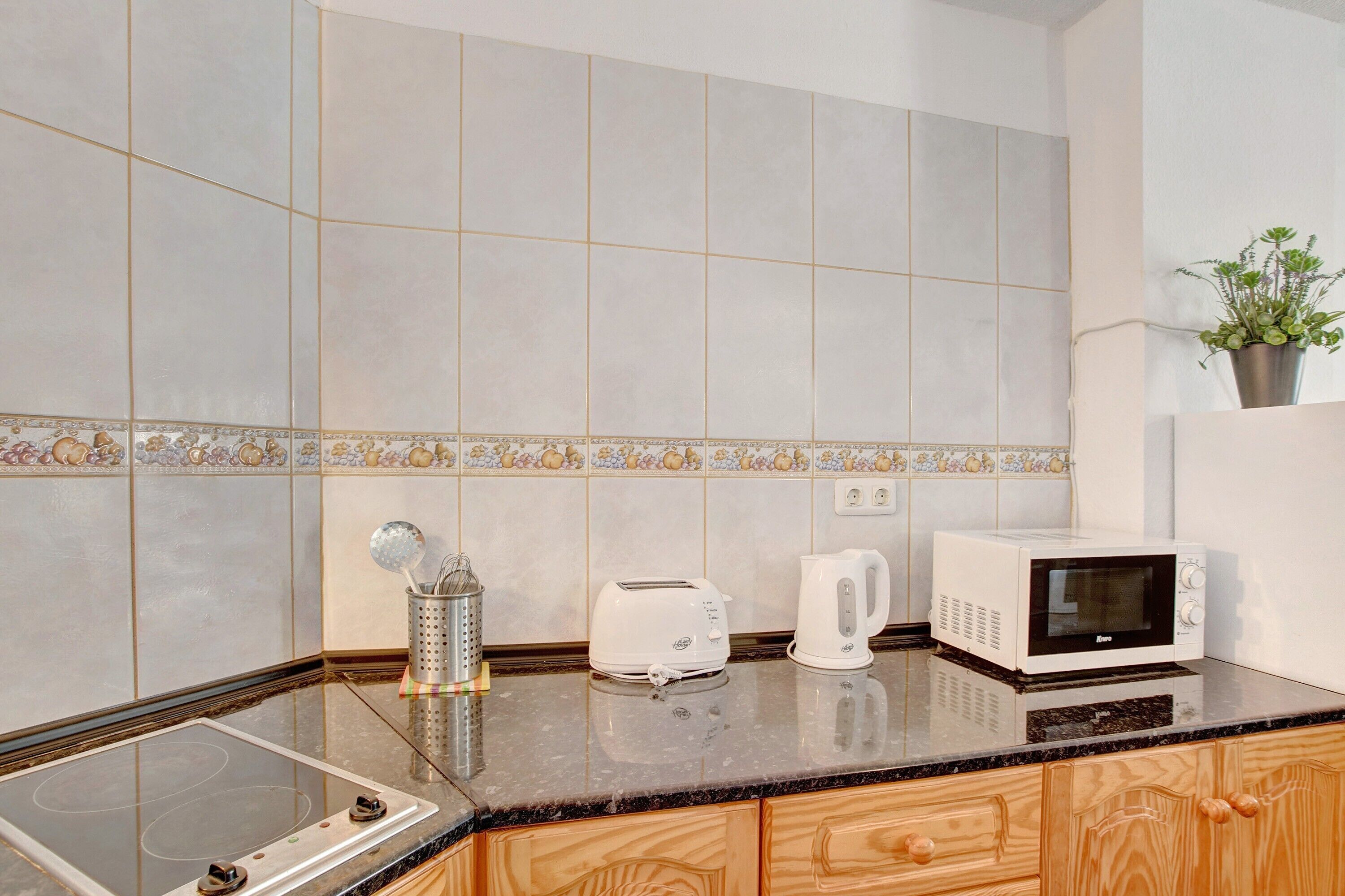 A kitchen with a stove, toaster, kettle, and microwave on the counter.