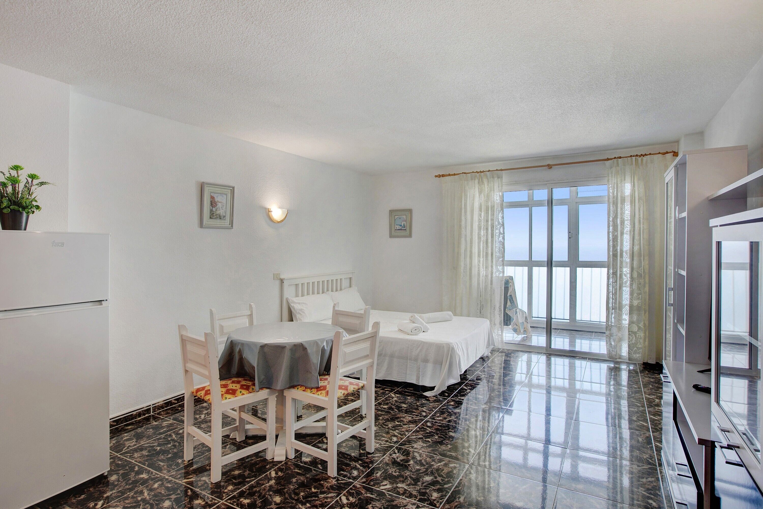 Una habitación con una cama, una mesa con sillas, un televisor y una ventana con cortinas.