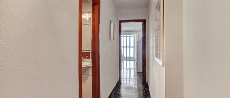 A hallway with a tiled floor, a wooden door, and a framed picture on the wall.