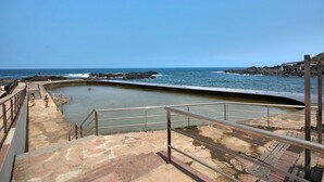 Un escalier en pierre mène à une piscine offrant une vue sur l’océan et la côte rocheuse.