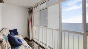 Un balcon avec vue sur la mer, un canapé avec des coussins et un rideau à rayures.