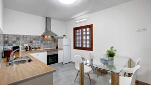 Eine moderne Küche mit einer zentralen Kochinsel, weißen Schränken, einer gefliesten Spritzschutzwand und einem Fenster mit Holzrahmen.