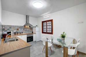 Une cuisine moderne dotée d’un îlot central, de meubles blancs, d’un pare-feu en carrelage et d’une fenêtre avec des cadres en bois.