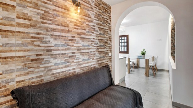 Ein modernes Interieur mit einer gemusterten Ziegelwand, einem dunklen Sofa und einem Essbereich mit Tisch und Stühlen.