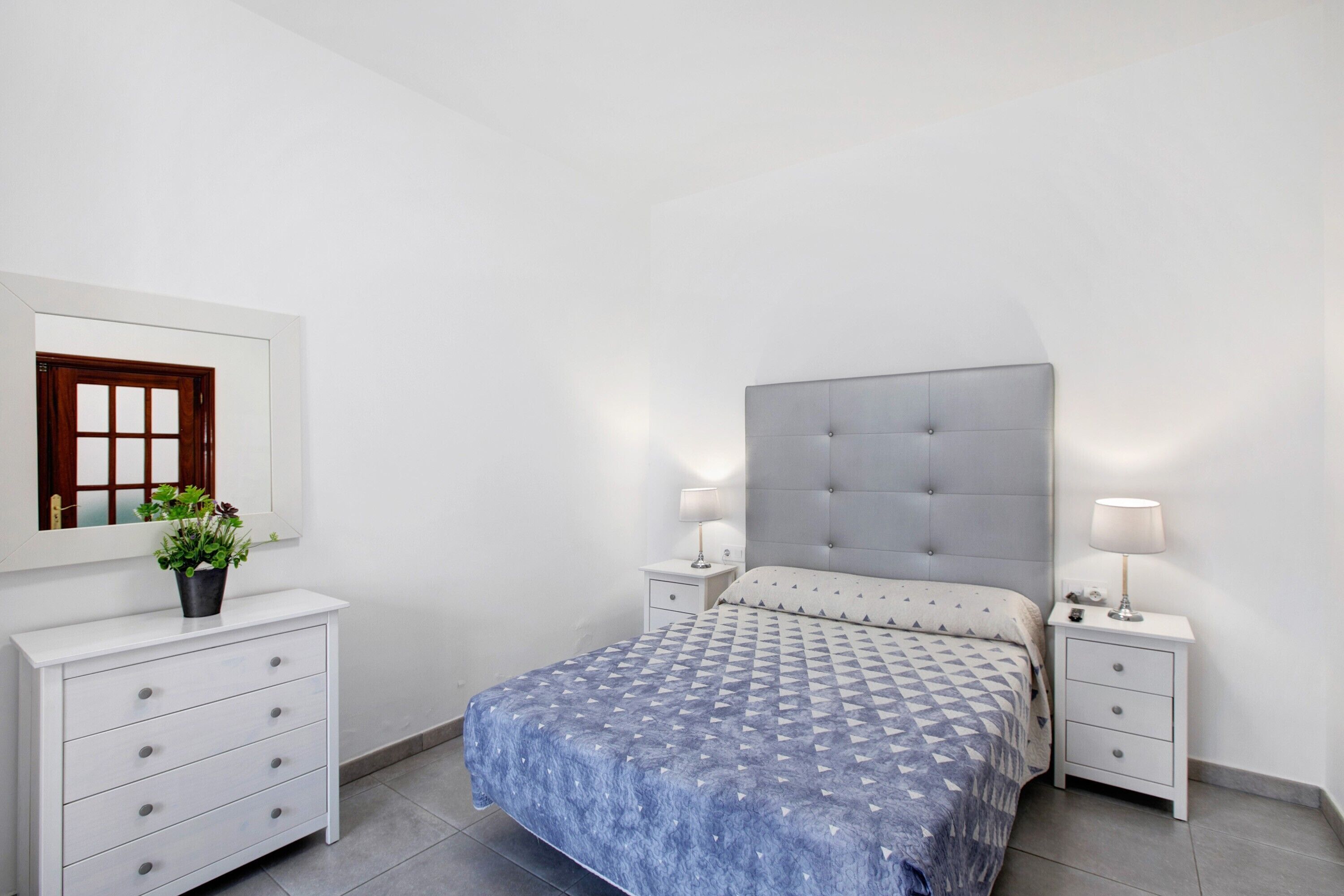 Ein Schlafzimmer mit Bett, Nachttischen, einem Schminktisch und einem Blumentopf.