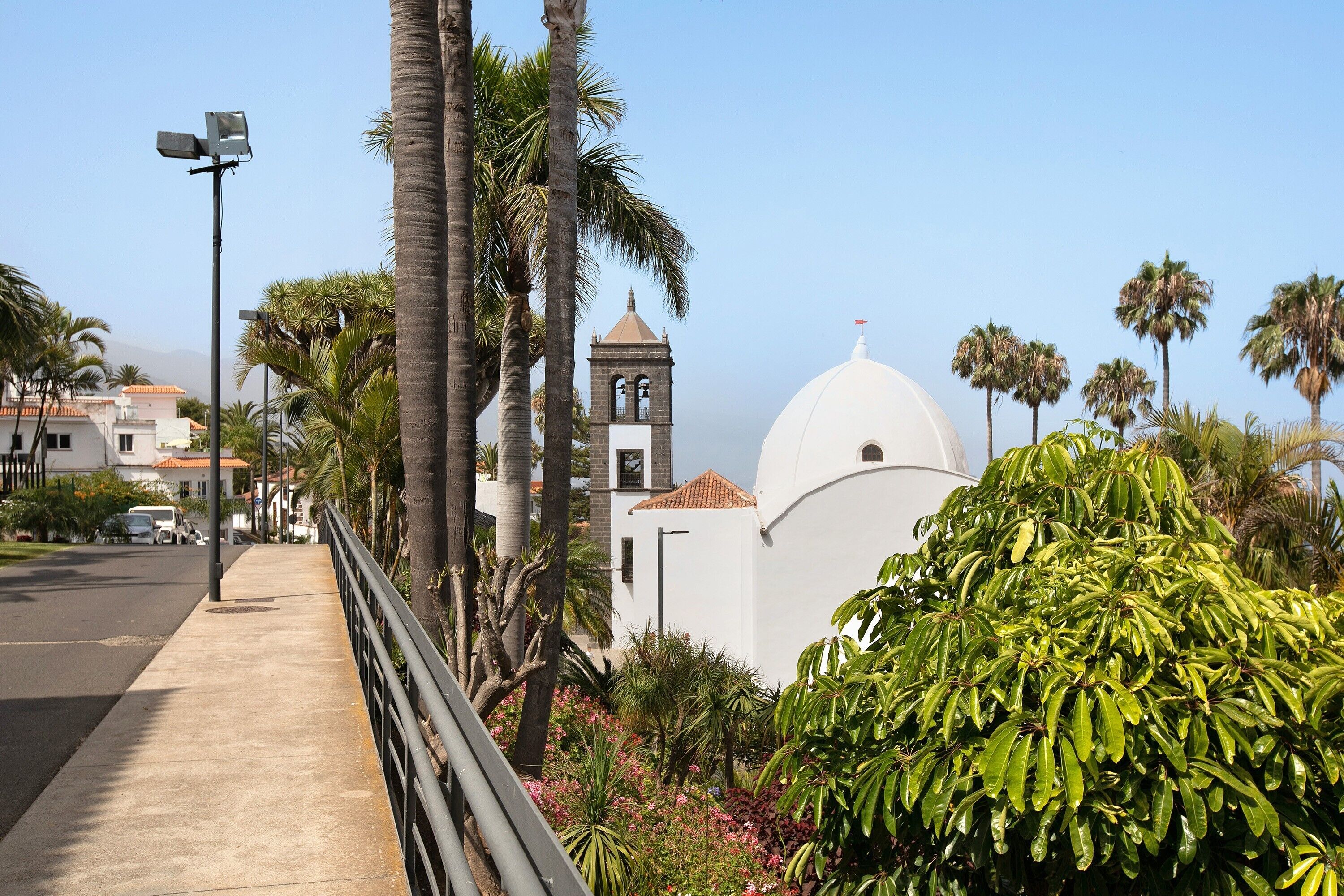 Una calle costera con una iglesia blanca, palmeras y cielo despejado.
