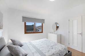 A bedroom with a bed, a dresser, a mirror, and a window with a view of buildings. - Vacation Home 'Casa Micaela 2' with Sea View, Terrace, Balcony & Wi-Fi (El Sauzal)