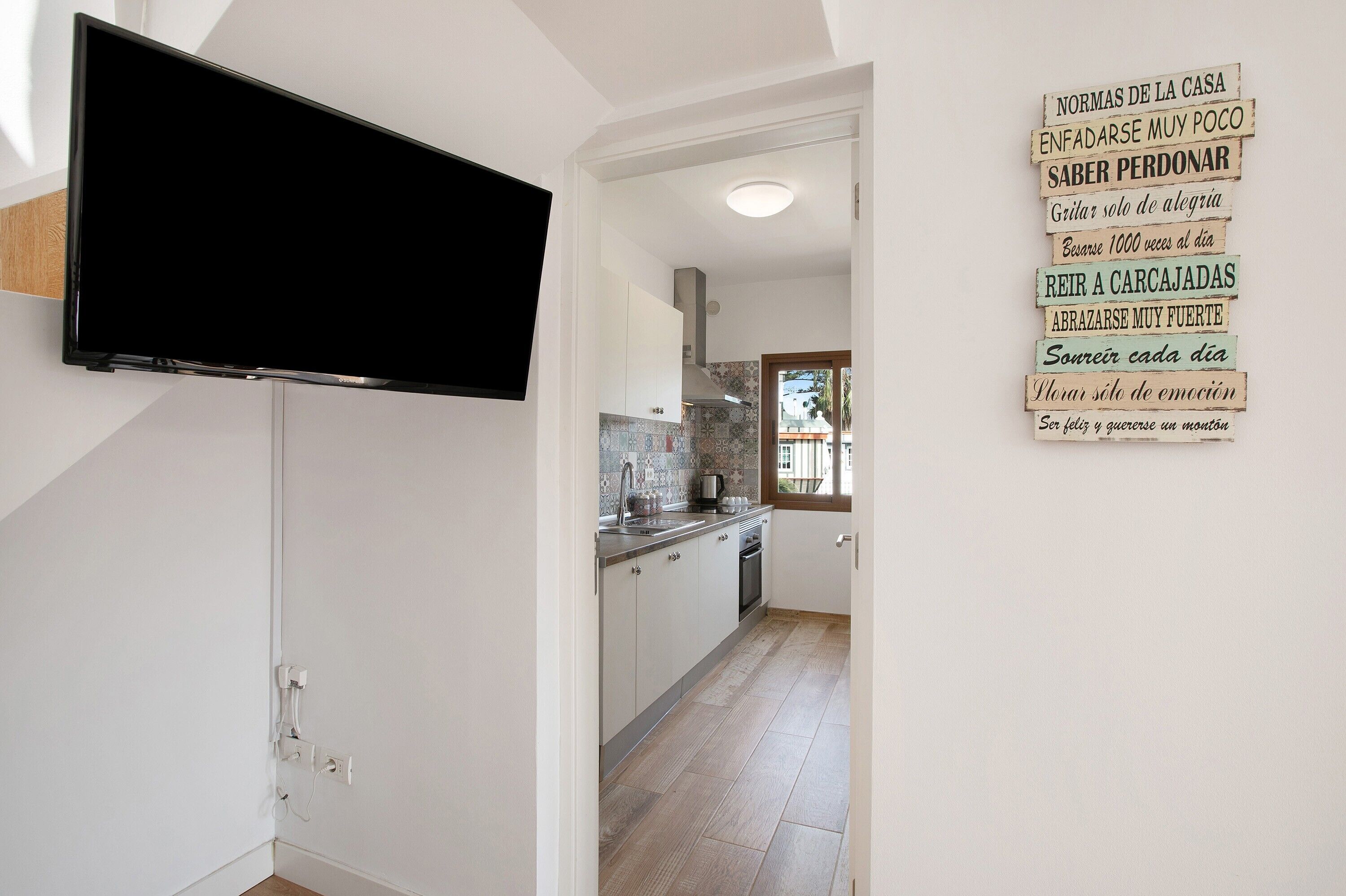Una cocina con armarios blancos, un televisor negro montado en la pared y salpicadero de azulejos.