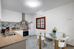 Een moderne keuken met een centraal eiland, witte kasten, een betegelde spatwand en een raam met houten kozijnen.