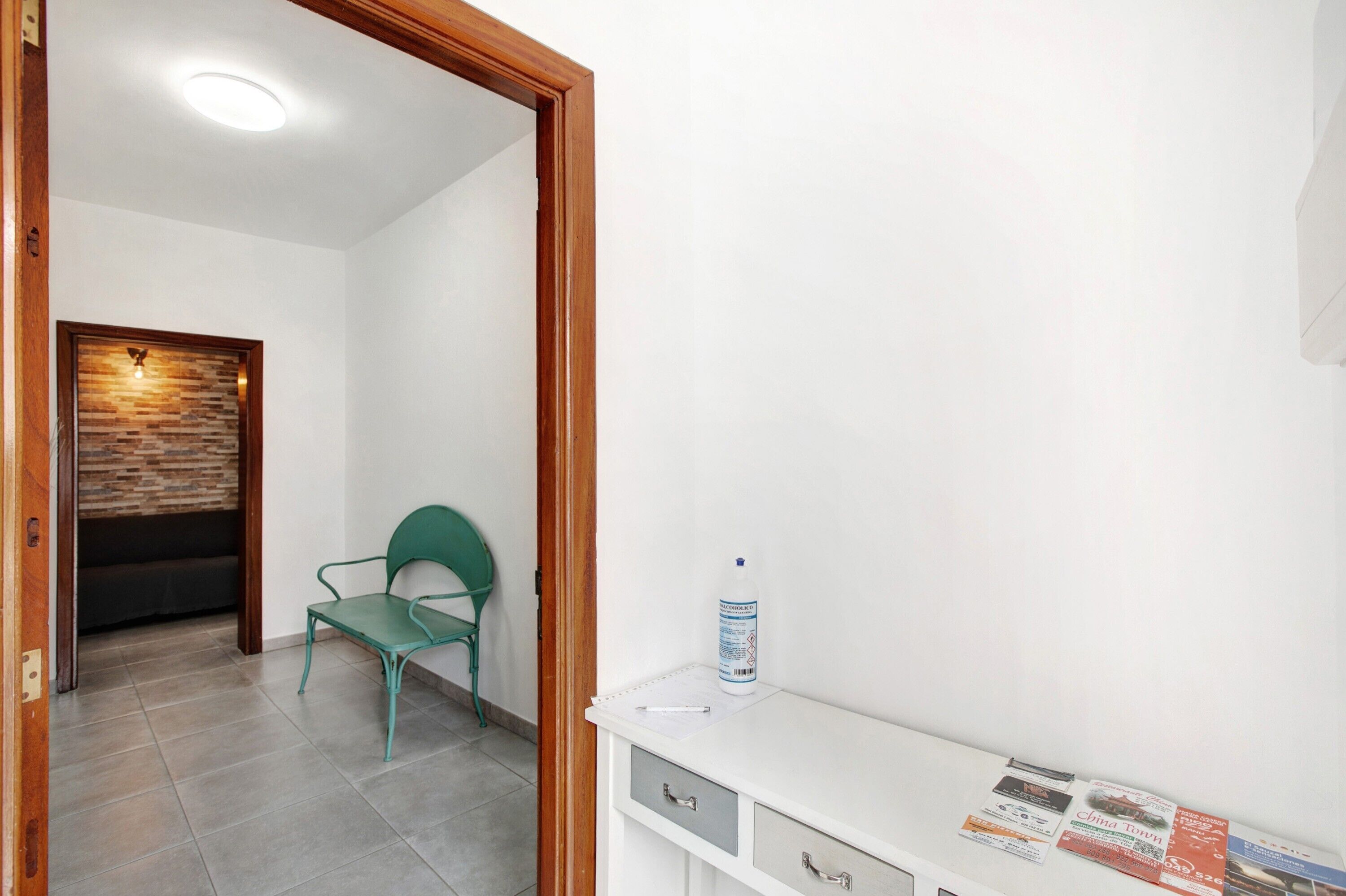 Una habitación con una silla verde, un escritorio blanco con papeles y un dispensador de gel antibacterial.