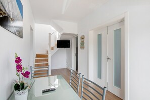 Een eethoek met een glazen tafel, stoelen, een afstandsbediening en een potorkidee.