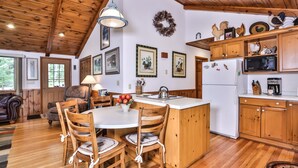 A cozy kitchen with wooden cabinets, a central island, and a dining area with wooden chairs. - Stepaway Vacation Rentals- Schneider Cabin (Sayner)