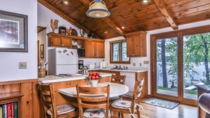 A wooden cabin interior with a kitchen, dining area, and large windows overlooking a forested area. - Stepaway Vacation Rentals- Schneider Cabin (Sayner)