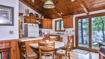 L’intérieur d’un chalet en bois comprend une cuisine, un coin repas et de grandes fenêtres donnant sur une zone boisée.