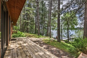 Eine Holzterrasse führt zu einer Seehütte mit Blick auf hohe Kiefern und einen stillen See.