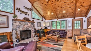 A cozy cabin interior with a stone fireplace, leather furniture, and wooden beams. - Stepaway Vacation Rentals- Schneider Cabin (Sayner)