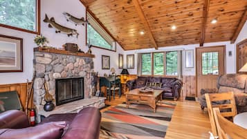 A cozy cabin interior with a stone fireplace, leather furniture, and wooden beams.