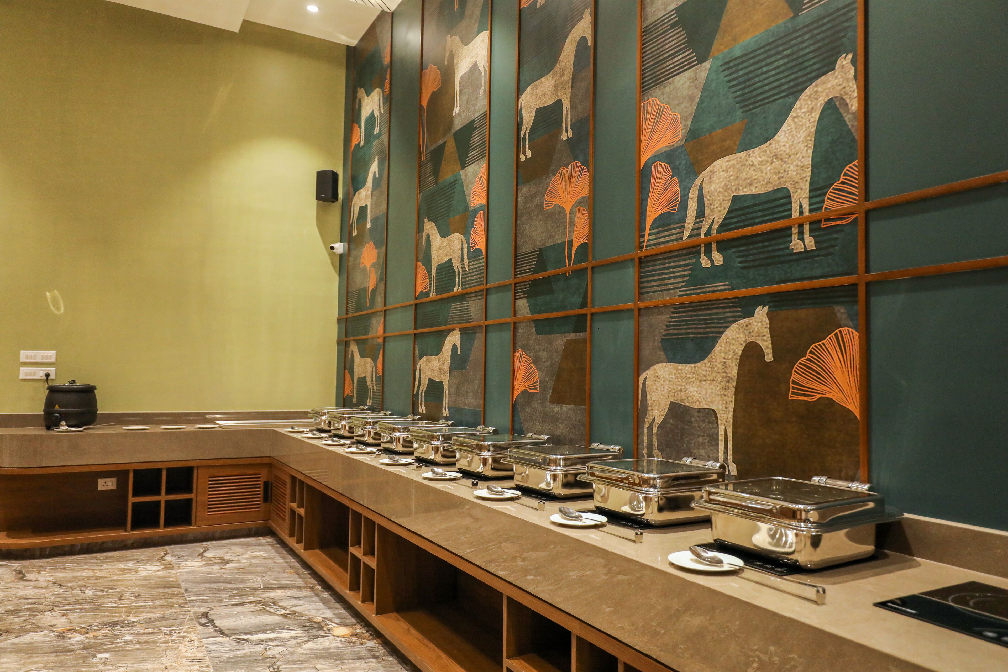 Montaje de bufé con múltiples estaciones de servicio, suelo de mármol y una pared decorativa con motivos de caballos y abanicos.