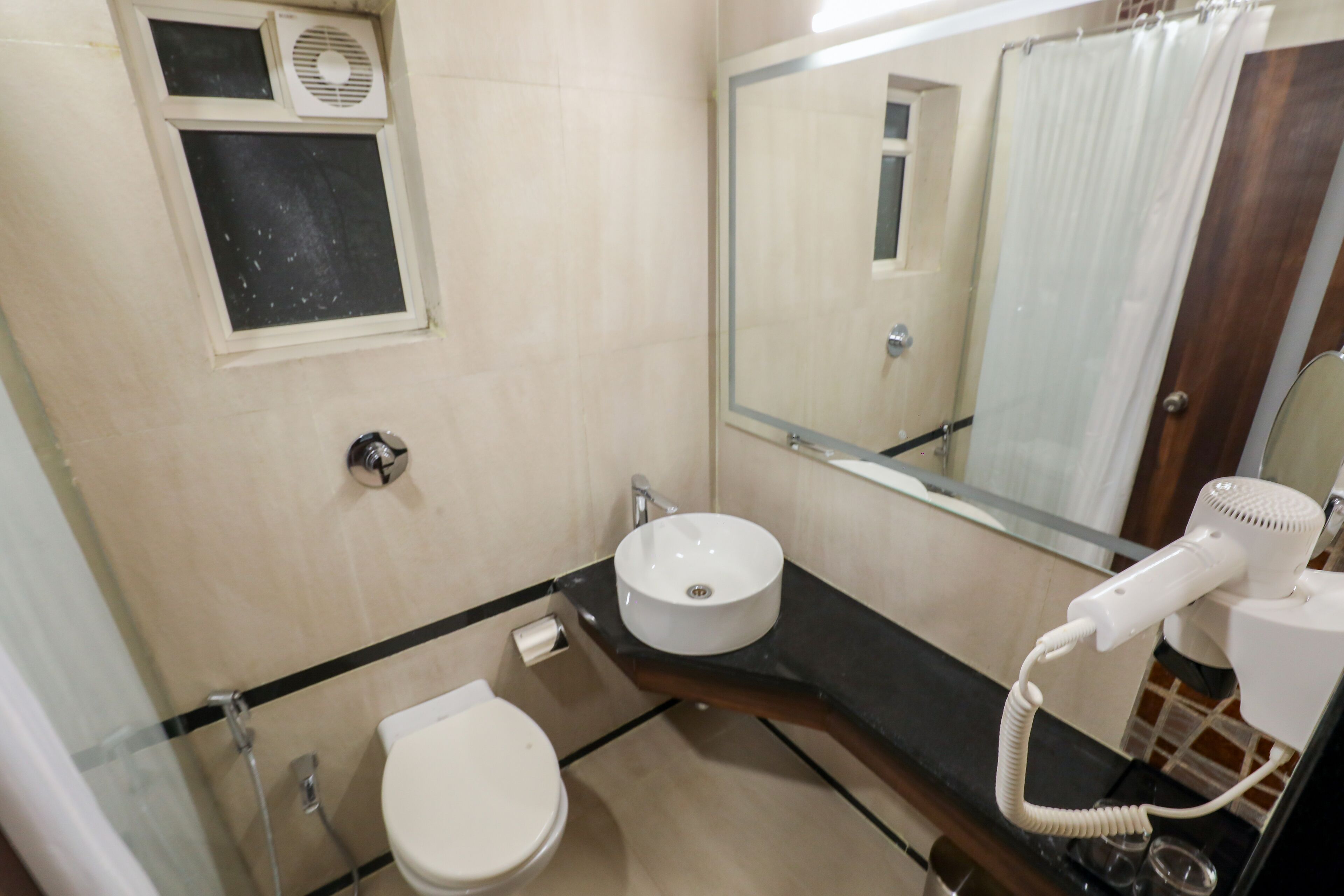 Un baño con inodoro, lavamanos, espejo y secador de pelo.