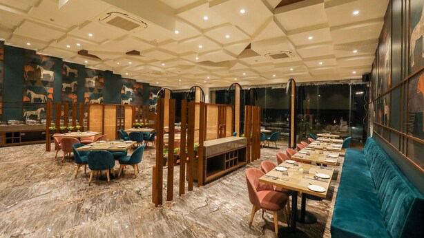 Ein Restaurant mit Marmorboden, Holzwänden und blau-rosa Stühlen. Die Tische sind mit Tellern und Gläsern gedeckt.