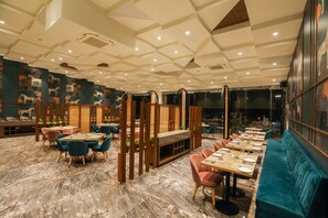 A restaurant with a marble floor, wooden partitions, and blue and pink chairs. Tables are set with plates and glasses. - Spree Hotel Aurangabad (Chhatrapati Sambhajinagar)
