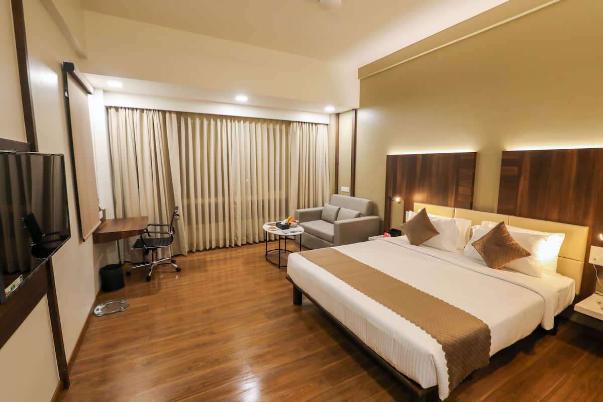 Une chambre d’hôtel avec un grand lit, un bureau, une chaise, une télévision et une fenêtre avec des rideaux.