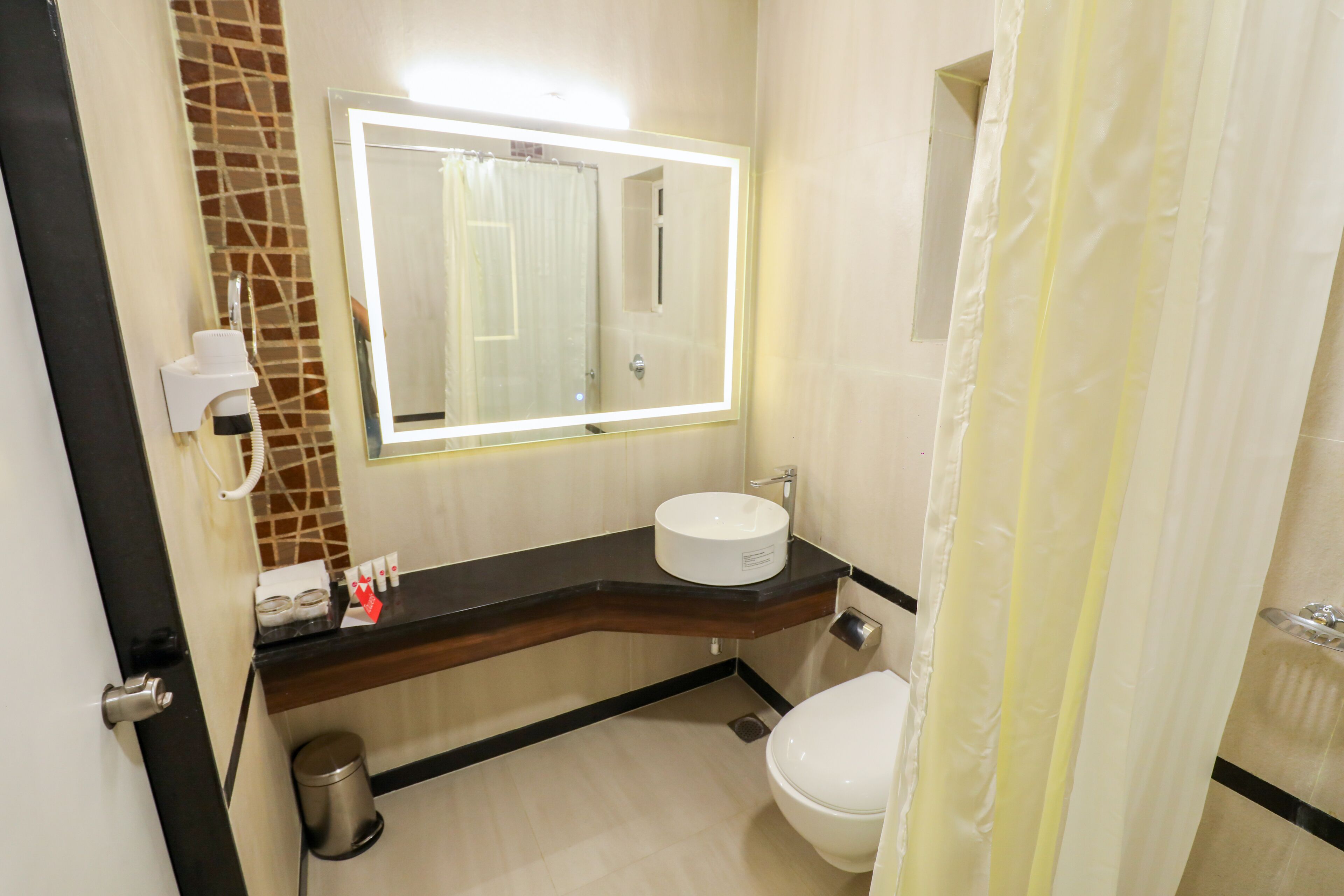 A bathroom with a white sink, a mirror with lights, a toilet, and a shower curtain.