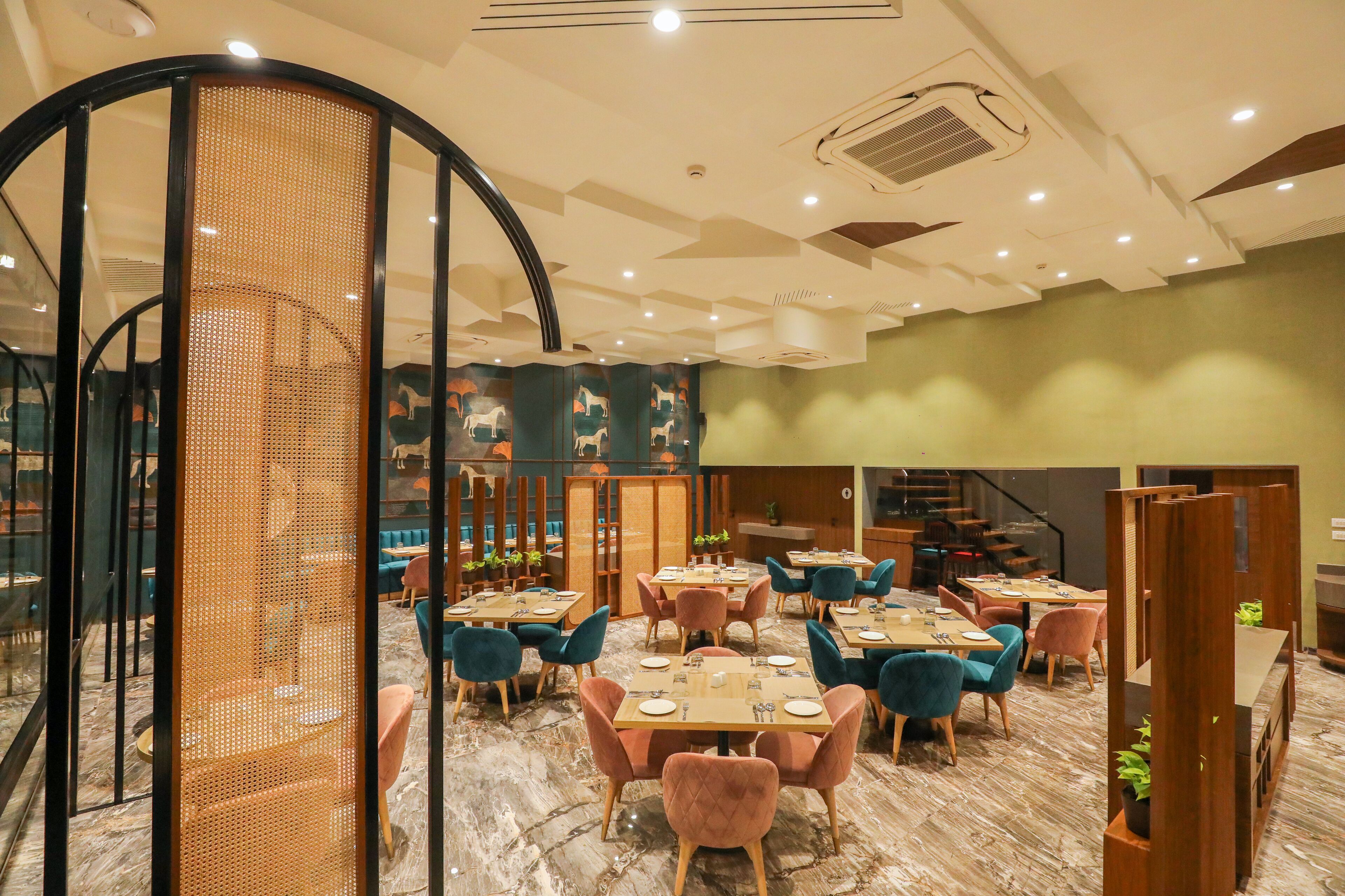 Un interior de restaurante moderno con mesas redondas, sillas acolchadas y un separador decorativo de madera.