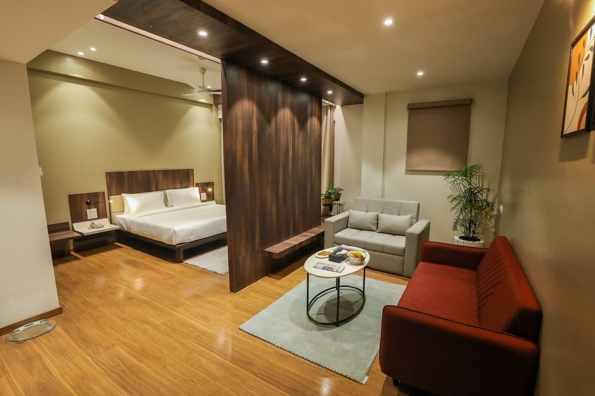 Une chambre d’hôtel moderne avec un plancher en bois, un lit recouvert de draps blancs, un canapé rouge, une petite table basse ronde et une plante en pot.