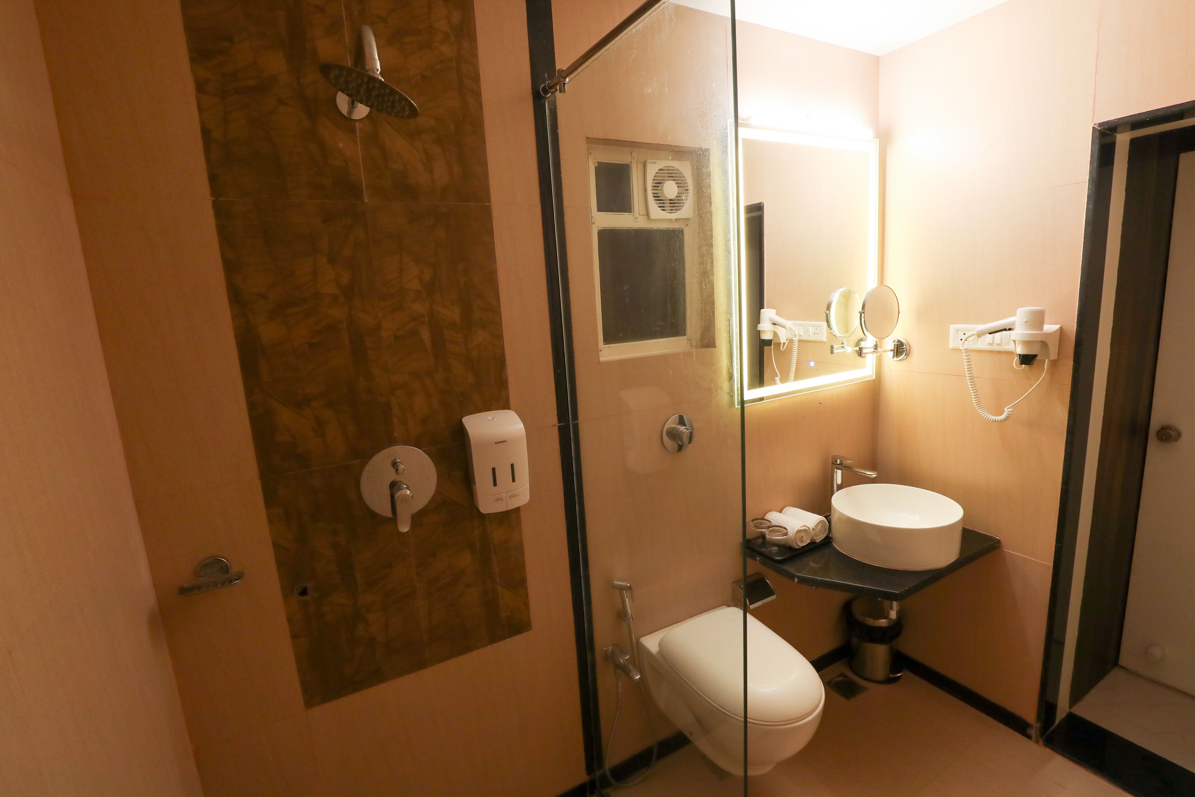 Un baño pequeño con ducha de vidrio, inodoro, lavabo con espejo y secador de pelo en la pared.