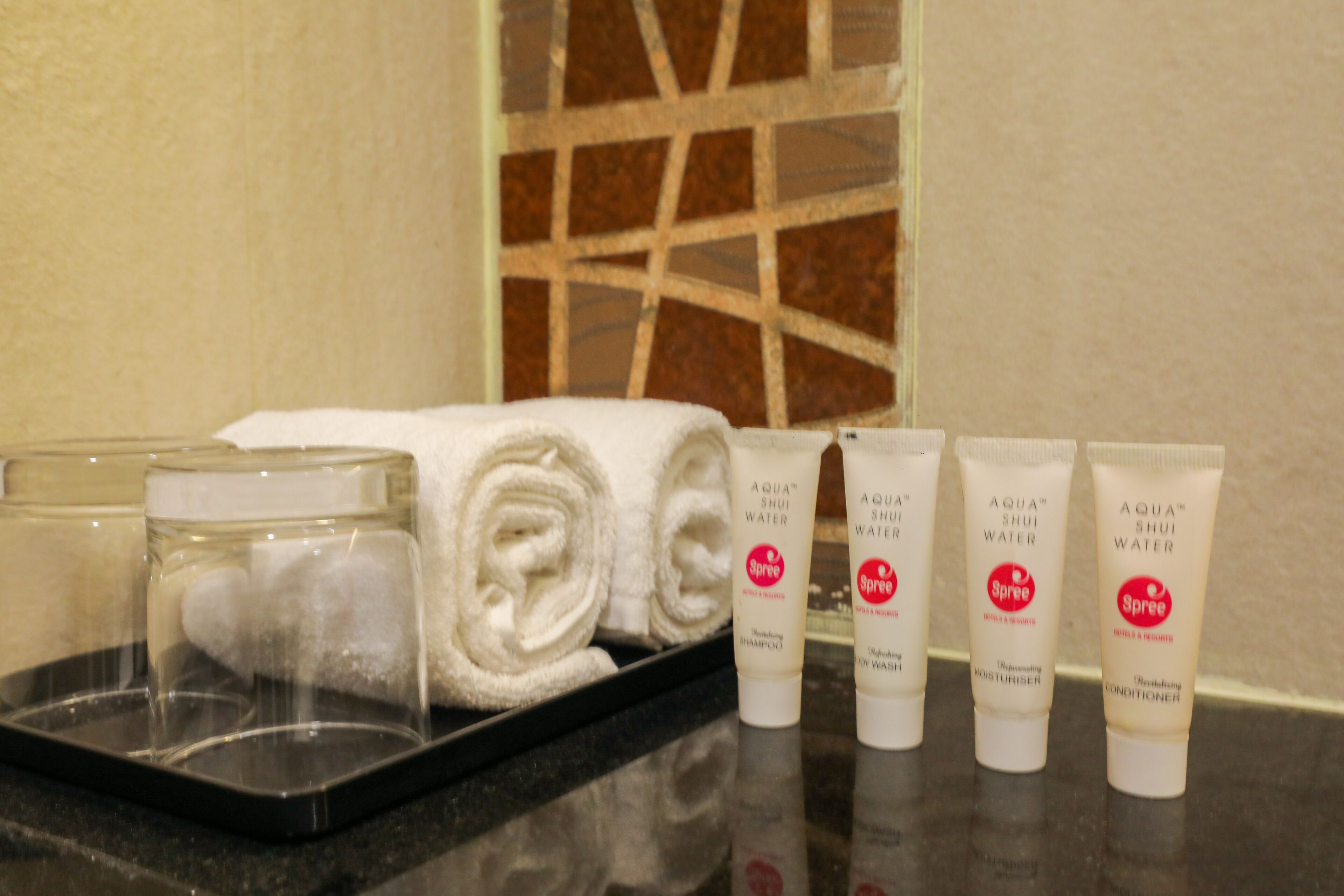 Una encimera de baño con artículos de aseo, incluyendo un vaso, toallas enrolladas y cuatro tubos de productos Aqua Shui Water.
