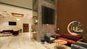 Eine geräumige Lobby mit Marmorboden, einem roten Sofa, einem grauen Sessel und einem runden Spiegel, der den Raum widerspiegelt.