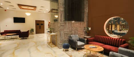 Un hall amplio con suelo de mármol, un sofá rojo, un sillón gris y un espejo redondo que refleja la estancia.